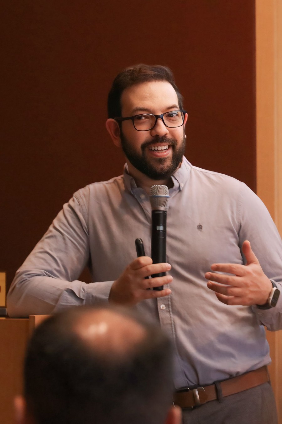 Mayron Piccolo speaking to an audience, microphone in hand
